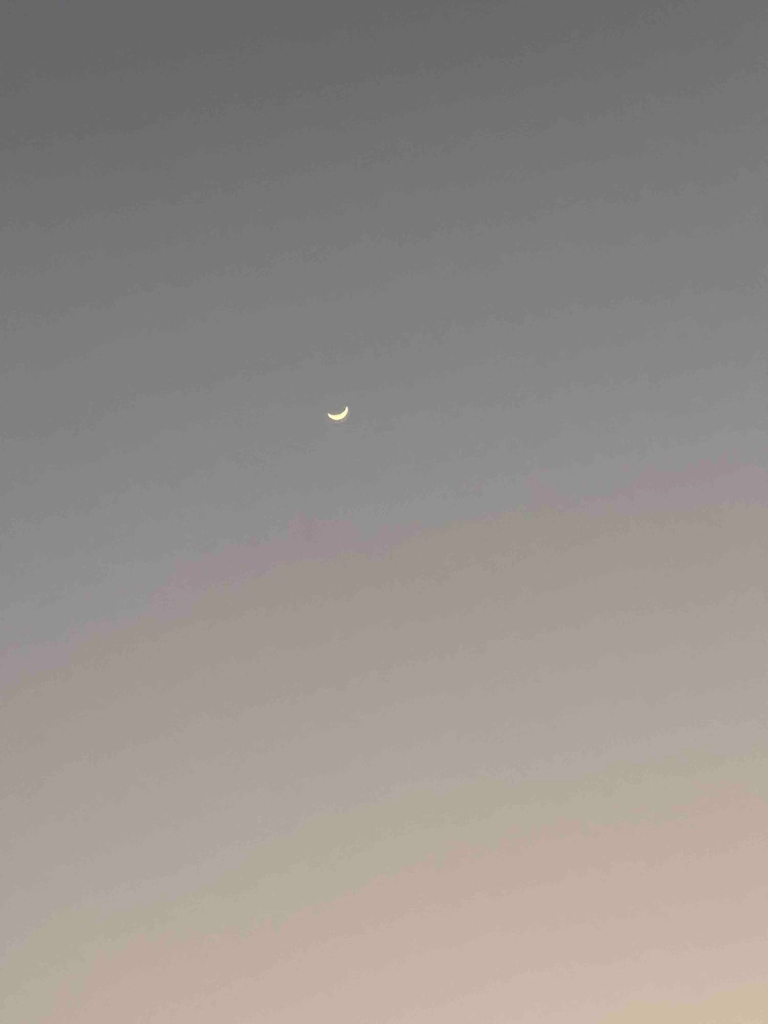 Crescent moon suspended in the fading light, colors beginning their daily retreat