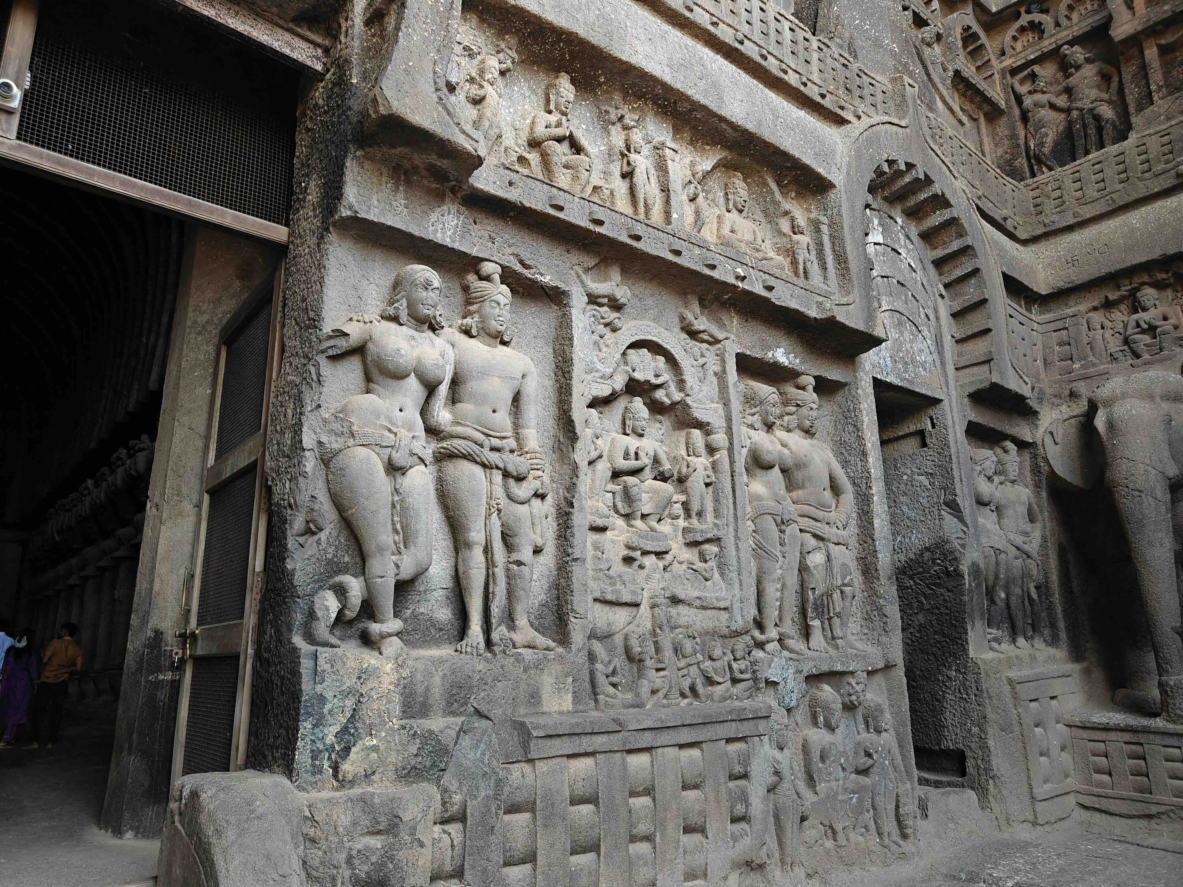 Carved couples in relief flank a central panel with a seated figure beside the doorway of the Karle Chaitya Griha, with an elephant at the far right.
